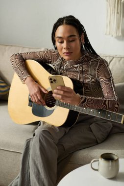 Süslü örgüleri olan genç bir siyahi kadın gitar çalarken evde rahatlıyor..