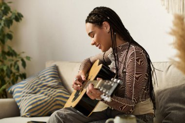 Örgülü genç bir Afrikalı Amerikalı kadın modern dairesinde gitar çalıyor, neşe saçıyor..
