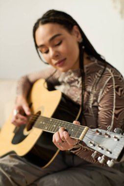 Genç bir Afrikalı Amerikalı kadın gitarını ışık dolu şık bir dairede tıngırdatıyor..