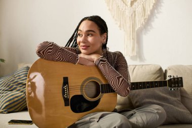 Canlı genç bir kadın koltuğunda uzanır, gitarını elinde tutar, rahat dairesinde gülümser..