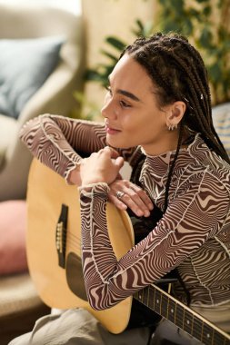 Örgülü genç bir zenci kadın rahat bir evde gitar çalarak rahatlıyor..