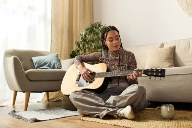 Saçları örgülü genç bir Afrikalı Amerikalı kadın şık yaşam alanında gitar çalmaktan hoşlanıyor..