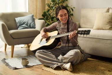 Genç bir Afrikalı Amerikalı kadın, sıcaklıkla çevrili şık evinde mutlu bir şekilde gitar çalıyor..