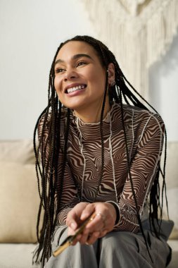 Saçları örgülü neşeli genç bir kadın şık dairesinde rahatlıyor, mutluluk saçıyor..