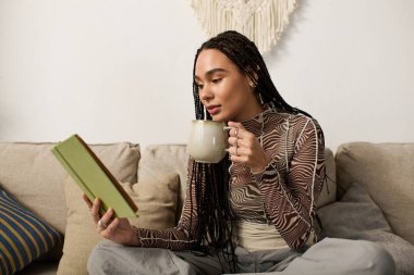 Şık bir dairede, genç bir Afrikalı Amerikalı kadın elinde sıcak bir içecekle okumaktan zevk alıyor..