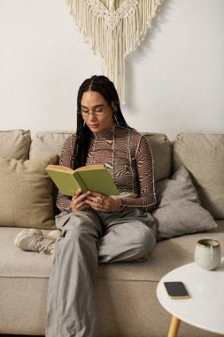 Genç bir Afrikalı Amerikalı kadın şık dairesinde kitap okumaktan zevk alıyor, sakin bir anı kucaklıyor..