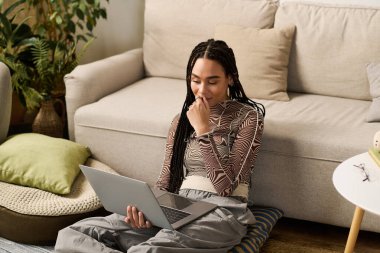 Genç bir Afrikalı Amerikalı kadın dizüstü bilgisayarıyla uğraşırken şık dairesinde dinleniyor..