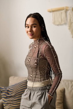 Süslü örgüleri olan genç siyahi bir kadın şık dairesinde zarif bir şekilde duruyor..