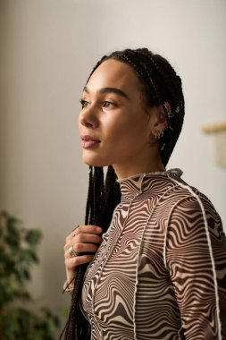 Saçları örgülü genç bir Afrikalı Amerikalı kadın şık bir dairede şık kıyafetine hayran..