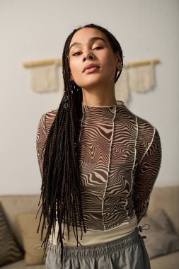 Süslü örgülü genç bir Afrikalı Amerikalı kadın modern dairesinde şık bir görünüm sergiliyor..