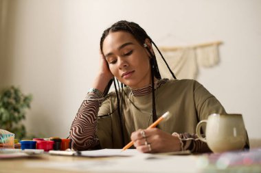 Örgülü genç bir Afrikalı Amerikalı kadın modern bir dairede sanatsal süreçten zevk alıyor..