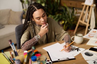 Örgülü genç bir kadın, rahat, modern bir apartman atmosferinde çizim yapmaya odaklanmış..