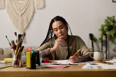 Saçları örgülü genç siyahi kadın sanat malzemeleriyle dolu şık dairesinde özenle çizimler yapıyor..