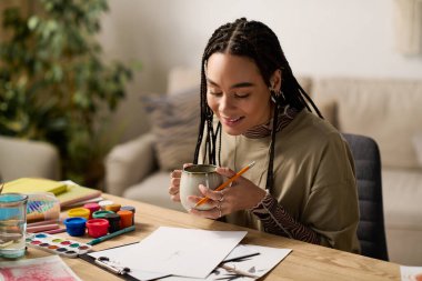 Genç bir kadın şık dairesinde oturuyor, içmekten ve resim yapmaktan zevk alırken gülümsüyor..