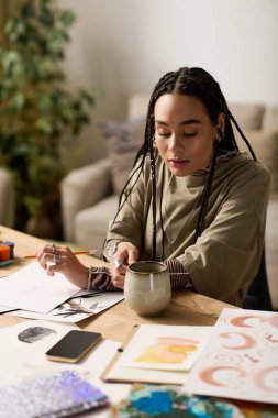 Genç bir Afrikalı Amerikalı kadın, çay içerken şık bir dairede vakit geçirmekten zevk alıyor..