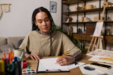 Örgülü genç bir kadın, rahat bir dairede çizim yaparken yaratıcılığını ifade eder..