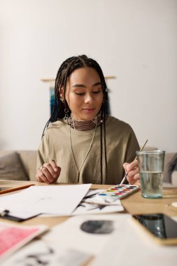 Dairesinde örgüleri olan, sanatla çevrili genç siyahi bir kadın..