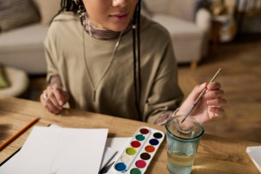 Genç siyahi bir kadın şık evinde canlı sanat malzemeleriyle yaratıcı bir şekilde resim yapıyor..