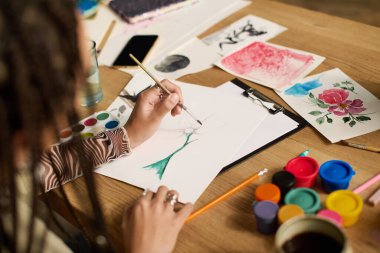 Saçları örgülü genç bir kadın şık dairesinde canlı bir şekilde resim yapıyor..