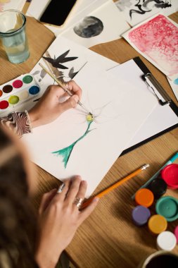 Şık giyinmiş genç bir kadın mutfak masasında resim yapıyor..