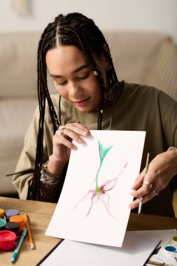 Örgülü genç kadın canlı suluboya resmini gururla evinde sergiliyor..