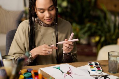 Modern bir dairede, örgülü genç bir kadın neşe içinde renkli sanatlar çiziyor, yaratıcılığı kucaklıyor..