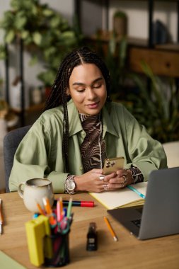 Genç bir kadın şık dairesinde oturuyor, telefonuna odaklanmış, etrafı canlı dekorlarla çevrili..