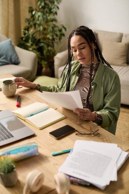 Genç siyah bir kadın gazete okuyor ve rahat dairesinde ahşap bir masada çay yudumluyor..