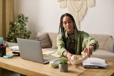 Süslü örgüleri olan genç bir Afrikalı Amerikalı kadın parlak dairesinde çalışma alanını düzenliyor..