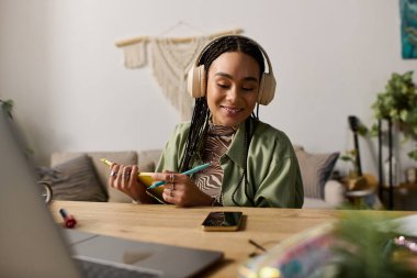 Şık bir dairede, saçı örgülü genç bir Afrikalı Amerikalı kadın yaratıcı bir şekilde çalışırken gülümsüyor..