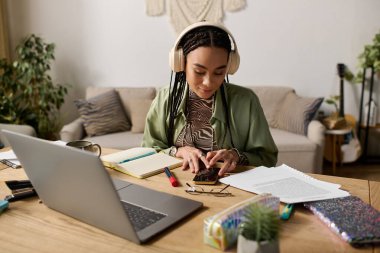 Saçları örgülü genç bir zenci kadın, etrafı notlar ve dizüstü bilgisayarla çevrili bir şekilde telefonuna çekiliyor..