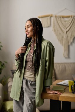 Kendine güvenen, örgülü siyah bir kadın şık dairesinde şık bir şekilde duruyor..