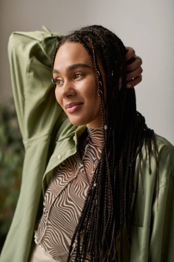 Saçları örgülü genç bir kadın moda evinde rahatlarken kendine güvenerek gülümsüyor..