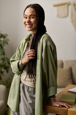 Güzel örgüleri olan genç bir Afrikalı Amerikalı kadın modern dairesinde dinlenirken gülümsüyor..