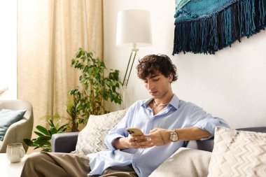 Genç adam akıllı telefonuna bakarken modern dairesinde rahatlıyor.