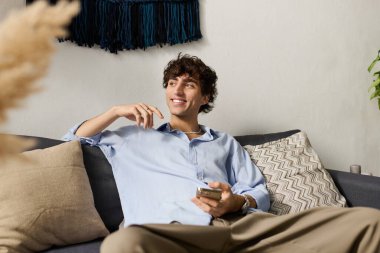 Mavi gömlekli genç adam şık dairesinde rahat bir şekilde oturur ve bir anlık mutluluğun tadını çıkarır..