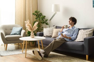 Kıvırcık saçlı şık genç adam evinde rahat rahat oturup sıcak bir içecek yudumluyor..