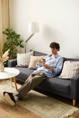 Kıvırcık saçlı yakışıklı genç bir adam evinde rahat bir kanepede keyif alıyor..