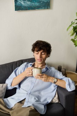 Kıvırcık saçlı genç adam evinde sıcak bir içecek yudumlarken rahatça dinleniyor..