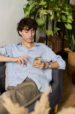 Yakışıklı genç adam rahat bir şekilde oturur, şık, rahat bir dairede telefonuna bakar..