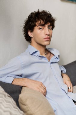 Kıvırcık saçlı genç adam şık bir dairedeki koltukta rahat bir şekilde dinleniyor, huzurun tadını çıkarıyor..