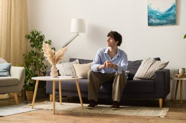 Genç bir adam lüks dairesindeki bir kanepede rahatça oturur, derin düşüncelerle..