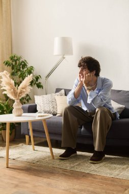 Yakışıklı genç adam düşünceli bir şekilde modern bir dairede oturuyor, etrafı hoş dekorlarla çevrili..