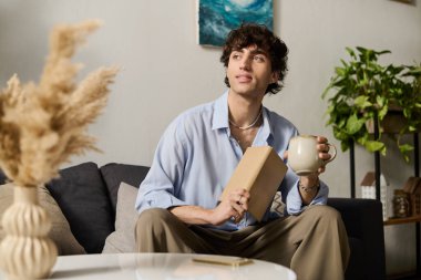 Kıvırcık saçlı yakışıklı genç adam modern dairesinde oturur, kahvesini yudumlar ve dinlenir..