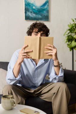 Kıvırcık saçlı yakışıklı genç adam modern yaşam alanında rahatça oturuyor, okumaya dalmış..