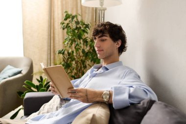 Yakışıklı genç adam şık dairesinde dinleniyor, büyüleyici bir kitapla çok meşgul..