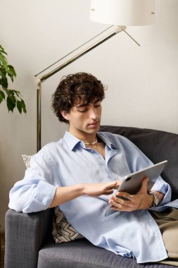Kıvırcık saçlı yakışıklı bir genç adam tabletle eğleniyor.