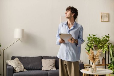 Mavi gömlekli yakışıklı genç bir adam çiçeklerle dolu modern bir dairede duruyor, gülümsüyor..