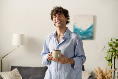 Kıvırcık saçlı yakışıklı genç adam modern dairesinde kahvesini yudumlarken mutlu hissediyor..