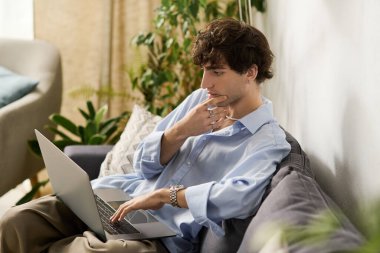 Kıvırcık saçlı genç adam laptopuyla şık bir iç mekanda derinden meşgul..